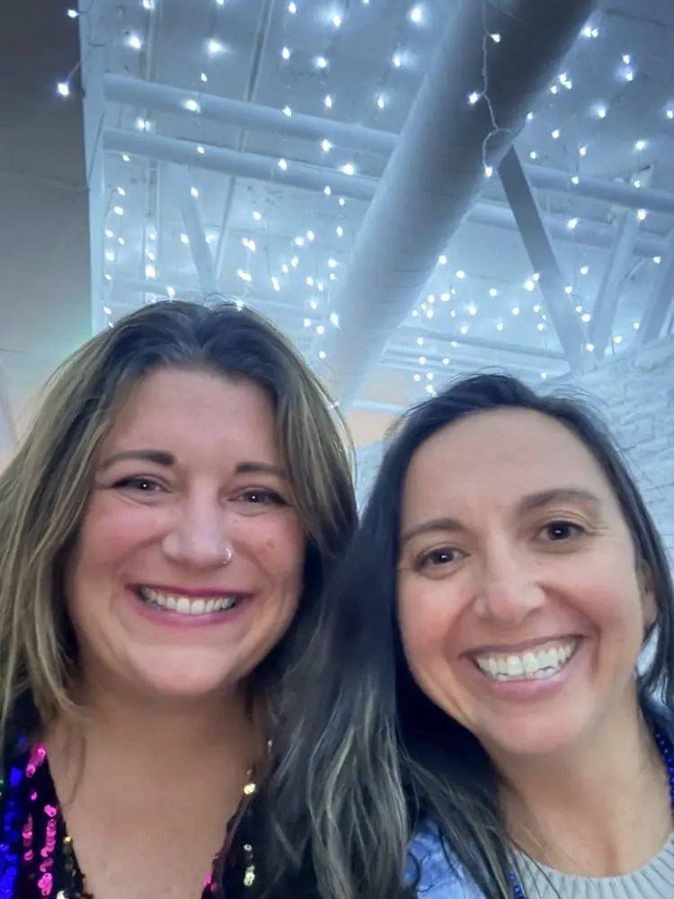 Val and a friend smiling in a selfie under string lights