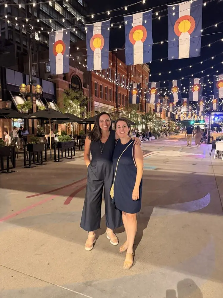 Val and a friend under strings of lights and Colorado flags on Larimer Square